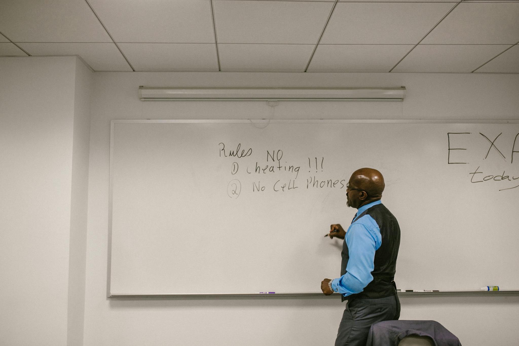 Instructor writing exam rules on a whiteboard in a college classroom.